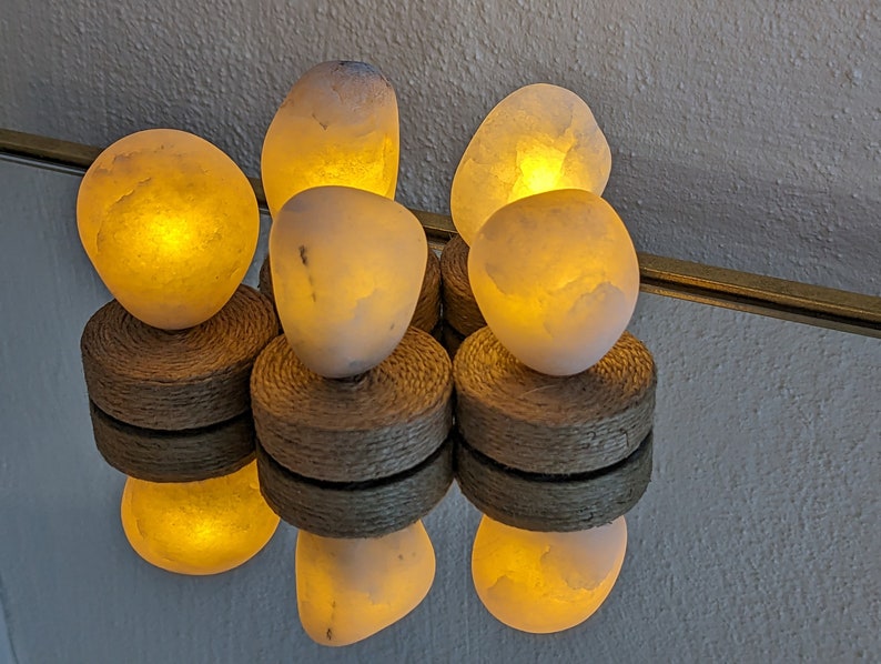 May include: Five white salt lamps with warm, glowing light, each sitting on a natural woven base.