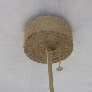 May include: A close-up of a ceiling light fixture made of natural rope, with a white cord hanging down.