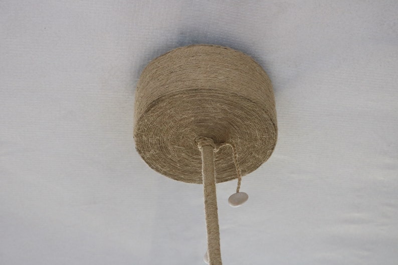 May include: A close-up of a ceiling light fixture made of natural rope, with a white cord hanging down.