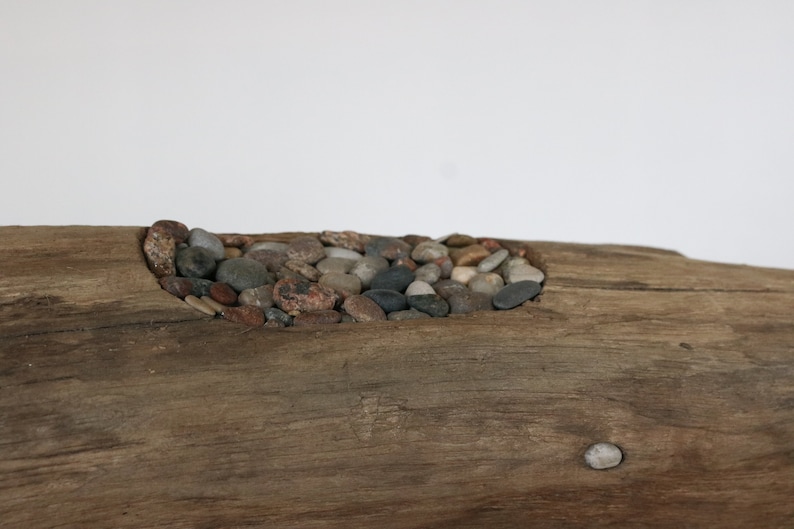 May include: A piece of driftwood with a carved out section filled with small, smooth stones of various colors.