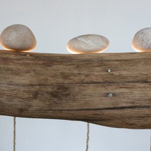 May include: A rustic wooden log with four smooth, round stones placed on top. Each stone has a small light underneath, creating a warm glow.