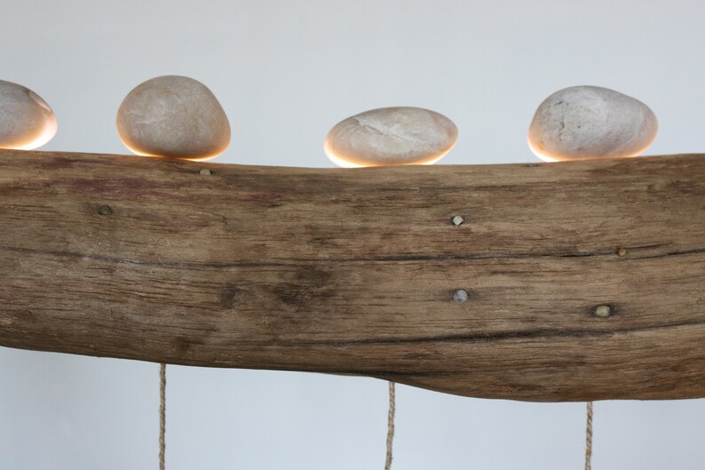 May include: A rustic wooden log with four smooth, round stones placed on top. Each stone has a small light underneath, creating a warm glow.