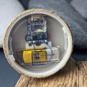 May include: A small, round, clear plastic container with a rope border. Inside the container is a small circuit board with wires and a yellow battery labeled "3.7V 450mAh 400mAh SEW ZEN CITY 42-01".