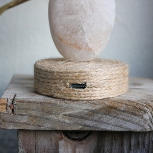 May include: A white salt lamp with a rope base sits on a wooden stand. The lamp has a charging port on the base.