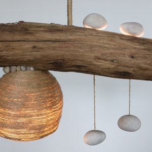 May include: A rustic wooden branch with a woven lampshade hanging from it. The branch is decorated with smooth white stones, some of which are hanging from the branch by strings.