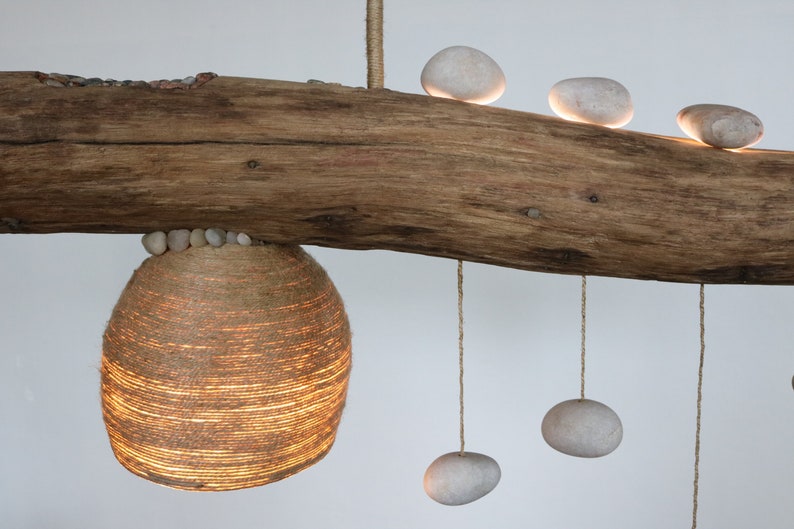 May include: A rustic wooden branch with a woven lampshade hanging from it. The branch is decorated with smooth white stones, some of which are hanging from the branch by strings.