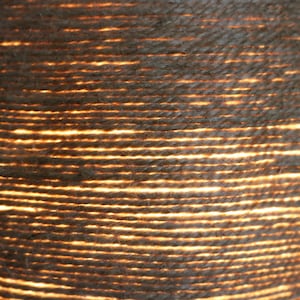 May include: Close-up of a woven lampshade made of natural fiber rope. The rope is tightly woven and the light shines through the gaps, creating a warm, inviting glow.