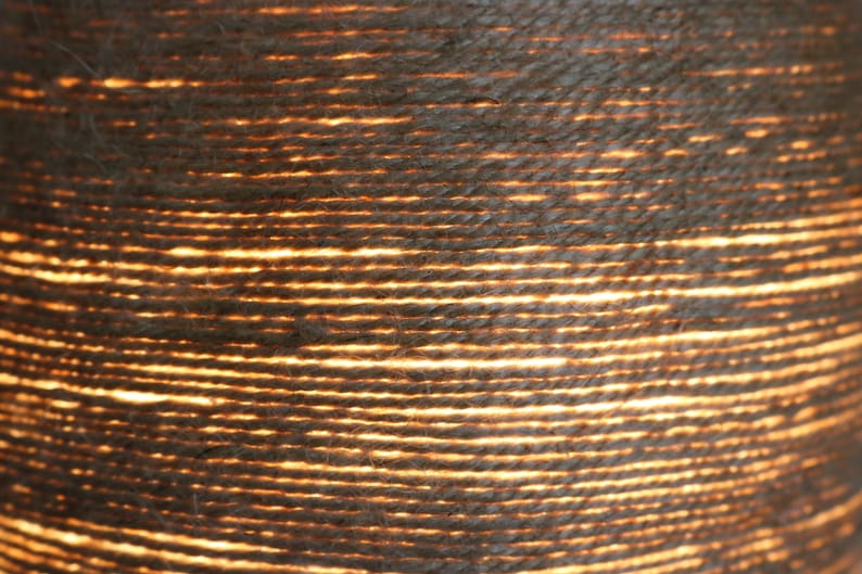 May include: Close-up of a woven lampshade made of natural fiber rope. The rope is tightly woven and the light shines through the gaps, creating a warm, inviting glow.