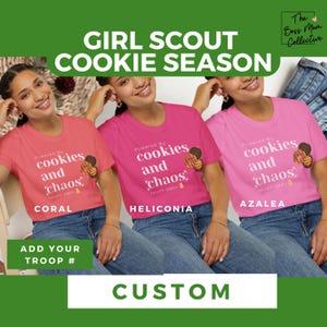 May include: Three women wearing pink, coral, and light pink t-shirts with the text "Powered by cookies and chaos" and a cookie graphic. The text "TROOP" and a number are below the graphic. The text "CORAL", "HELICONIA", and "AZALEA" are below the shirts. The text "ADD YOUR TROOP #" is below the shirts. The text "CUSTOM" is at the bottom of the image.
