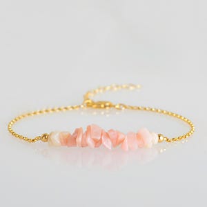 Puede incluir: Una delicada pulsera dorada con una cadena y un cierre, con una hilera de pequeñas piedras preciosas rosas irregulares. Las piedras preciosas son de un suave color rosa pastel. La pulsera tiene una fina cadena.