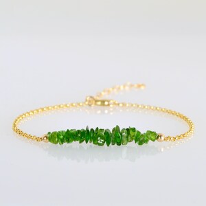 May include: A gold-coloured bracelet with a string of bright green gemstone chips. The bracelet has a fine chain design with a small gold bead at each end of the gemstone section. The clasp is adjustable.