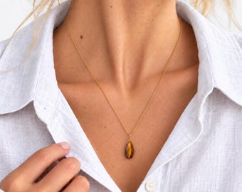 May include: A gold chain necklace featuring a teardrop-shaped tiger's eye gemstone pendant. The pendant displays a smooth, polished surface with characteristic brown and golden chatoyant bands, suspended from a delicate, thin gold-tone metal chain.