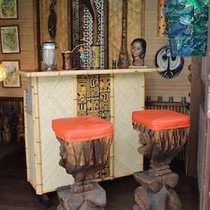 May include: Two tiki-style bar stools with orange cushions and carved wooden bases. The stools are in front of a bamboo bar counter with a tiki-themed design.