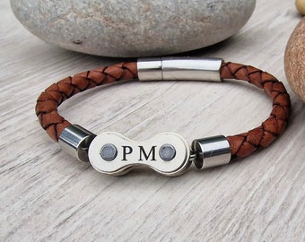 May include: Brown braided leather bracelet with a silver clasp and a decorative center piece. The center piece has the initials "PM" engraved on it. The bracelet is approximately 8 inches (20 cm) in length.