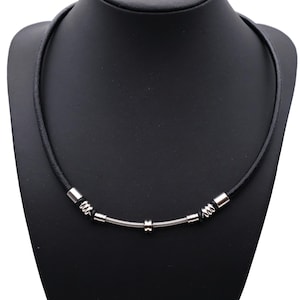 Peut inclure: Un collier en cuir noir avec des détails en métal argenté. Le collier présente un design à ressort hélicoïdal au centre, avec des détails cylindriques et enroulés en métal. Le collier est présenté sur un mannequin noir.