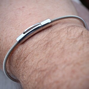 Pode incluir: Uma pulseira prateada com um design em espiral e um fecho seguro. A pulseira &eacute; usada no pulso, mostrando sua est&eacute;tica elegante e minimalista. O fecho &eacute; feito de metal brilhante e polido, adicionando um toque de eleg&acirc;ncia &agrave; joia.