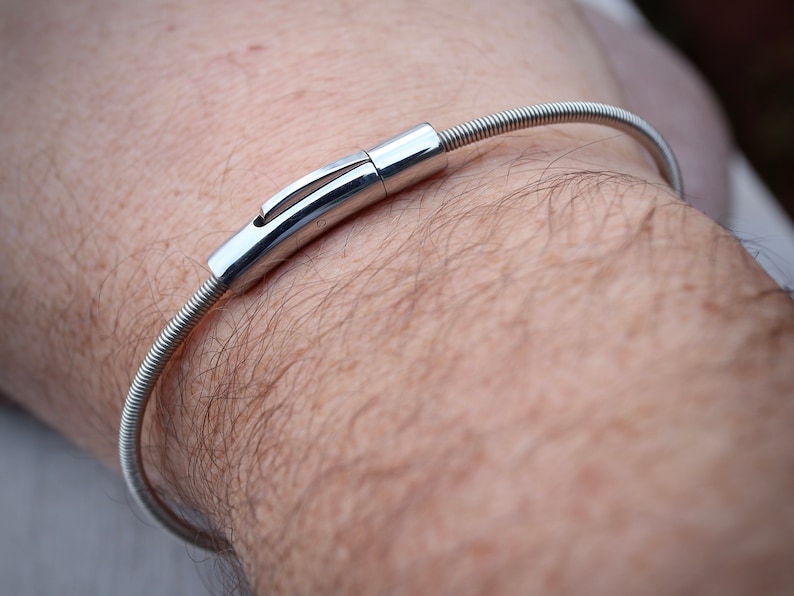 Pode incluir: Uma pulseira prateada com um design em espiral e um fecho seguro. A pulseira &eacute; usada no pulso, mostrando sua est&eacute;tica elegante e minimalista. O fecho &eacute; feito de metal brilhante e polido, adicionando um toque de eleg&acirc;ncia &agrave; joia.