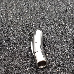 May include: Three magnetic jewelry clasps in silver and black. The clasps are cylindrical with a smooth, polished finish. The silver clasps are stainless steel, while the third clasp is black. The clasps are designed to connect jewelry pieces.