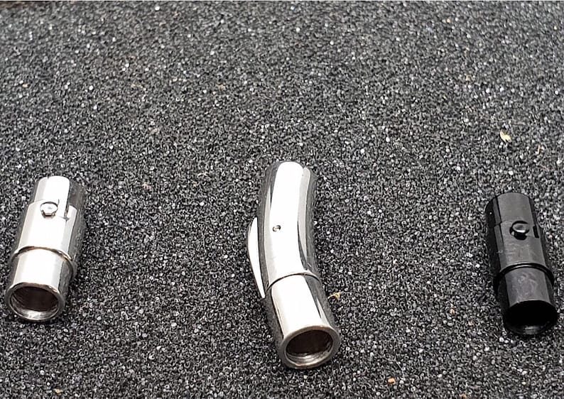 May include: Three magnetic jewelry clasps in silver and black. The clasps are cylindrical with a smooth, polished finish. The silver clasps are stainless steel, while the third clasp is black. The clasps are designed to connect jewelry pieces.