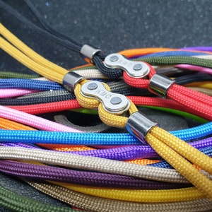May include: Close-up of a collection of colorful lanyards. Each lanyard features a braided cord in various colors, including yellow, red, blue, and green. The lanyards are connected with a metal clasp and metal ends. The clasp has the letters "KMC" on it.