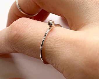 Peut inclure: Une bague en argent avec une petite boule sur le dessus. La bague est portée à un doigt.