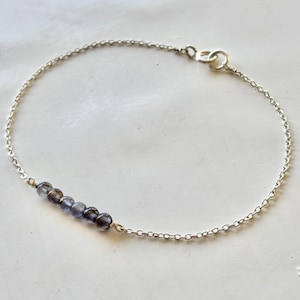 Può includere: Un delicato braccialetto d'argento con una serie di piccole perline rotonde blu scuro. Le perline sono infilate e attaccate a una sottile catena d'argento. Il braccialetto ha un design semplice ed elegante con chiusura a fermaglio.
