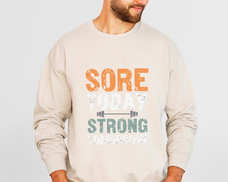 May include: A beige sweatshirt with the text "SORE TODAY STRONG TOMORROW" printed on the front. The text is in a distressed font with a green barbell graphic.