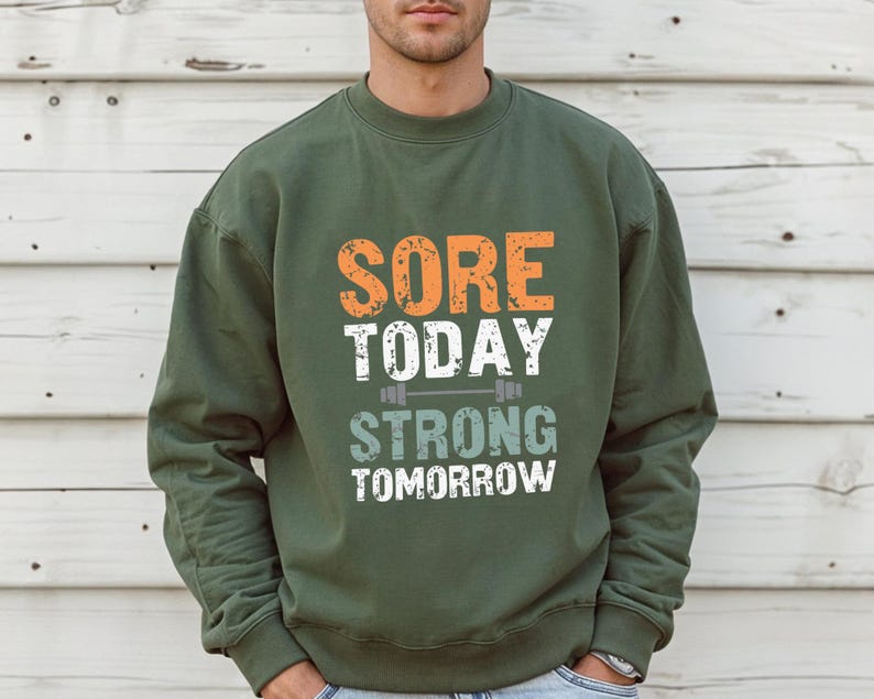 May include: Green sweatshirt with the text "SORE TODAY STRONG TOMORROW" in orange, white, and gray lettering. A small barbell graphic is above the word "STRONG".
