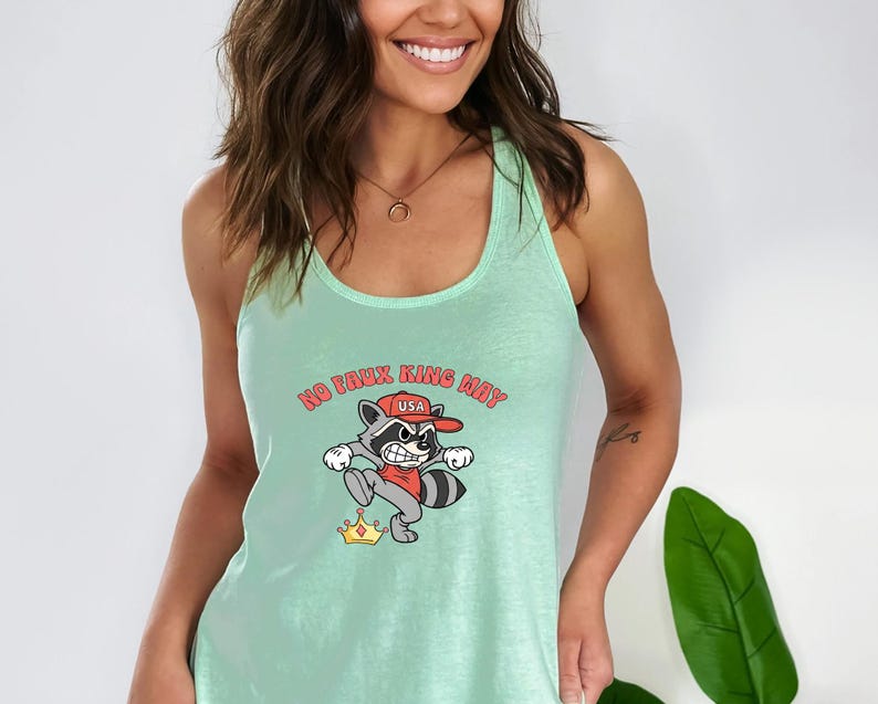 May include: A light green tank top with a cartoon raccoon graphic. The raccoon wears a red hat with "USA" on it and is stepping on a gold crown. The text "NO FAUX KING MAY" is above the raccoon.