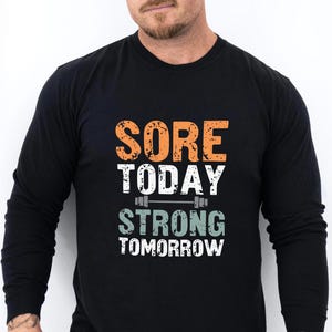 May include: Black long-sleeve shirt with the text "Sore Today Strong Tomorrow" in orange and green with a barbell graphic.