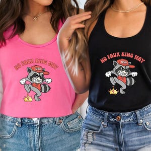 May include: Pink and black tank tops with a raccoon graphic. The raccoon wears a red hat and shirt, and a gold crown. The text "NO FAUX KING WAY" is above the raccoon. The raccoon graphic is on the front of the tank tops.