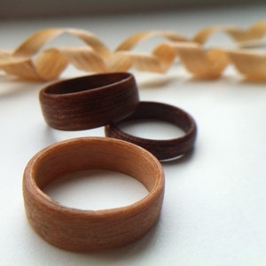 May include: Three wooden rings, one light brown and two dark brown, stacked on top of each other.