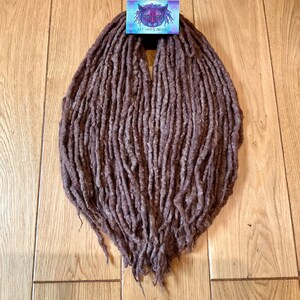 Könnte beinhalten: Ein Bündel brauner synthetischer Dreadlocks mit einem Etikett mit der Aufschrift "Cat Lady's Dreads".