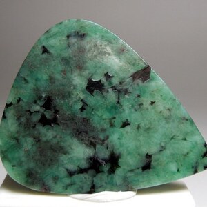 Peut inclure: Une pierre pr&eacute;cieuse d'&eacute;meraude verte avec des inclusions noires. La pierre pr&eacute;cieuse est taill&eacute;e en forme de larme et a une surface polie.