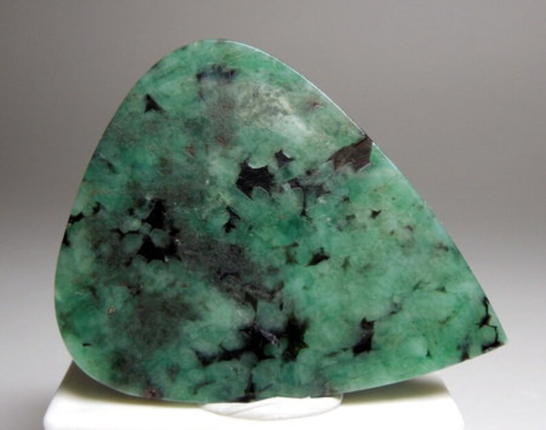 Peut inclure: Une pierre pr&eacute;cieuse d'&eacute;meraude verte avec des inclusions noires. La pierre pr&eacute;cieuse est taill&eacute;e en forme de larme et a une surface polie.