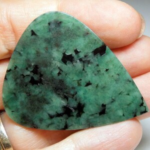 Peut inclure: Un cabochon d'&eacute;meraude verte avec des inclusions noires. La pierre est taill&eacute;e en forme de larme et a une finition polie.