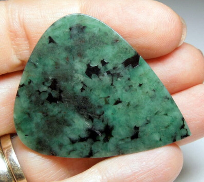 Peut inclure: Un cabochon d'&eacute;meraude verte avec des inclusions noires. La pierre est taill&eacute;e en forme de larme et a une finition polie.