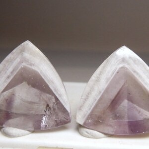 May include: Two triangular amethyst cabochons with a white, layered, translucent top and a purple, translucent base.