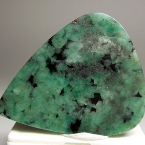 Peut inclure: Un cabochon d'&eacute;meraude verte avec des inclusions noires. La pierre est taill&eacute;e en forme de larme et a une surface lisse et polie.