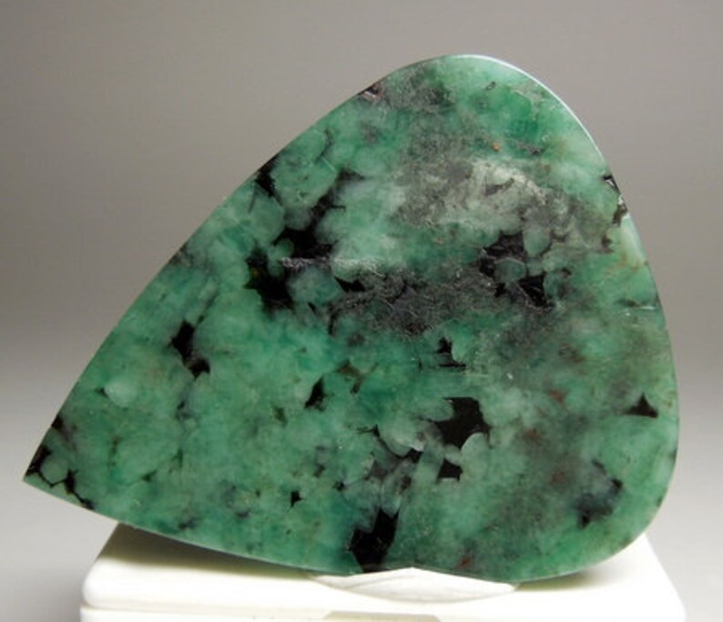Peut inclure: Un cabochon d'&eacute;meraude verte avec des inclusions noires. La pierre est taill&eacute;e en forme de larme et a une surface lisse et polie.