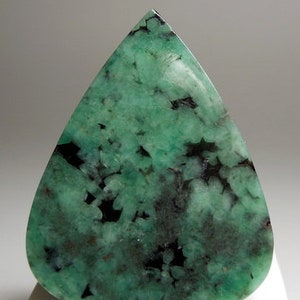 Peut inclure: Une pierre pr&eacute;cieuse cabochon d'&eacute;meraude verte avec des inclusions noires. La pierre est taill&eacute;e en forme de larme et a une finition polie.