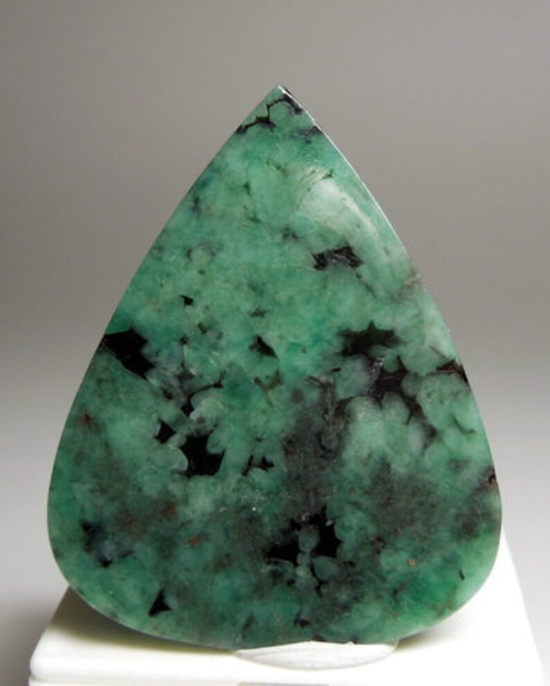 Peut inclure: Une pierre pr&eacute;cieuse cabochon d'&eacute;meraude verte avec des inclusions noires. La pierre est taill&eacute;e en forme de larme et a une finition polie.