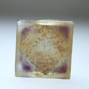 以下が含まれることがあります： 紫がかった色合いの透明な立方体状の結晶で、茶色の内包物が含まれています。結晶は半透明で、ざらざらとした質感の表面をしています。