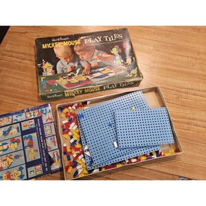 May include: Vintage Mickey Mouse Play Tiles set. The box features an illustration of children playing with the tiles. The set includes blue perforated tiles, colorful plastic pieces, and instruction cards. The box reads "MICKEY MOUSE PLAY TILES".