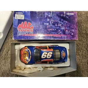 May include: A blue and red die-cast model race car with the number 66 on the side and hood, displayed in its original box. The box features the "MAC TOOLS Collector's Club" logo and a stadium scene.