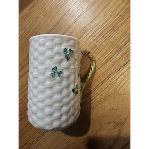 Può includere: Tazza in ceramica bianca con un motivo a intreccio e accenti di trifogli verdi. Il manico è dipinto per assomigliare a una vite. Una tazza decorativa per bevande.