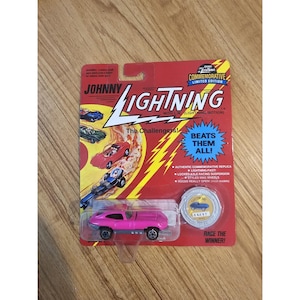 May include: A pink Johnny Lightning die-cast car on a red and yellow commemorative card. The card features the text "The Challengers!" and "Beats Them All!" The car is a replica with mag wheels.