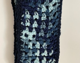 May include: A crocheted scarf in shades of blue and teal. The scarf is made with a simple stitch pattern and has a fringed edge.