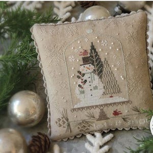 May include: A cross stitch pattern featuring a snowman in a snow globe with the text "Let It Snow!" and "With The New Year".