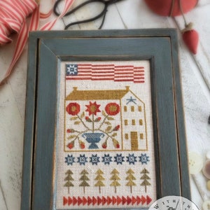 May include: A framed cross-stitch design of a house with a red, white, and blue American flag above it. The house is surrounded by flowers and trees. The frame is a dark blue color with a distressed finish. The text "THREAD WITH THY NEEDLE" is on the bottom right corner of the frame.